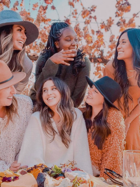 Group of friends laughing outdoors at a fall gathering, with warm autumn leaves and drinks on the table