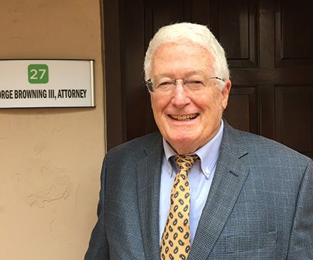 A man in a suit and tie is smiling in front of a sign that says george browning iii attorney.