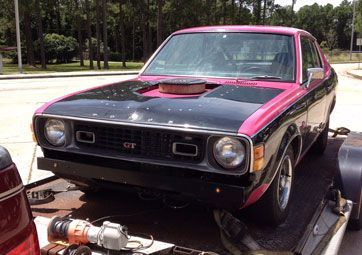 A pink and black car is sitting on top of a trailer.