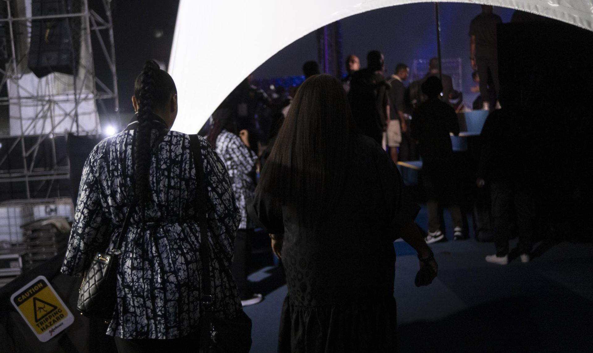 People walking in a dimly lit space with a large, bright arched light.