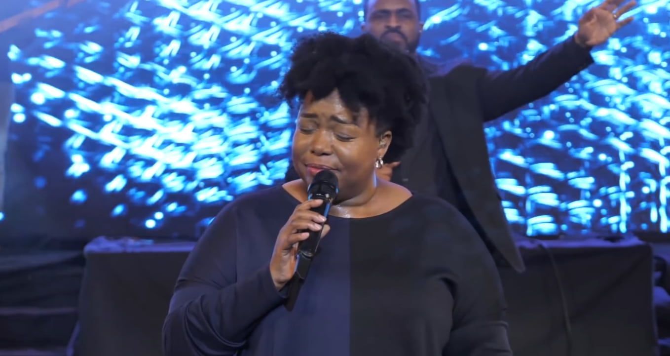 Chevelle singing into a microphone on stage, with a person in the background raising their arms. 