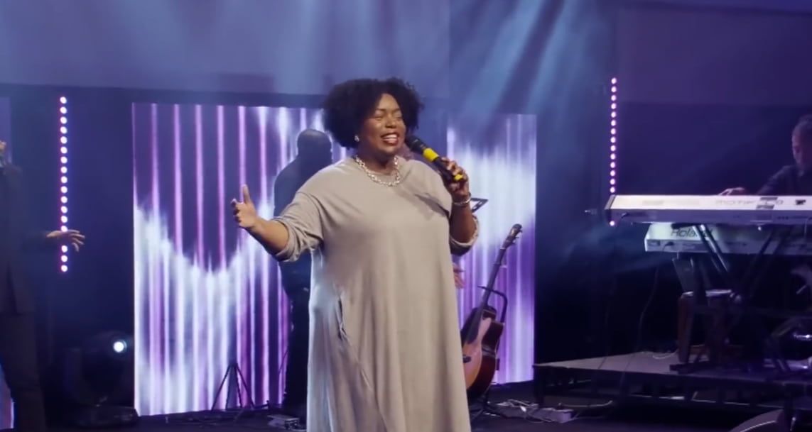 Chevelle singing on stage with microphone, performing in front of a band and light display.