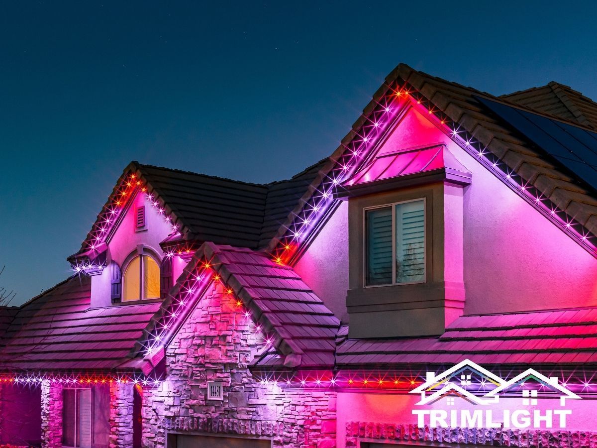 House with red and pink Trimlight roofline lights illuminated at night.