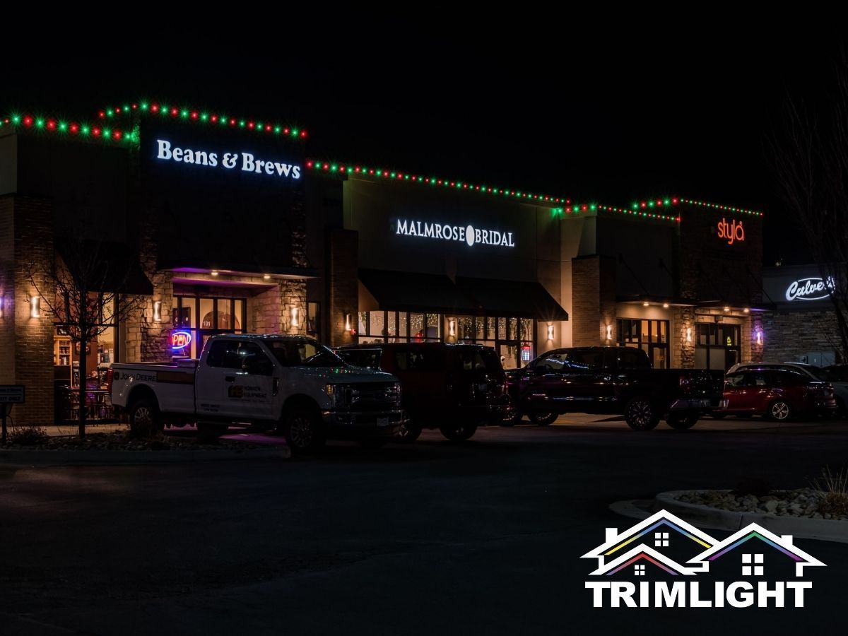 Businesses at night, decorated with red and green lights. Parked vehicles and TRIMLIGHT logo in the foreground.