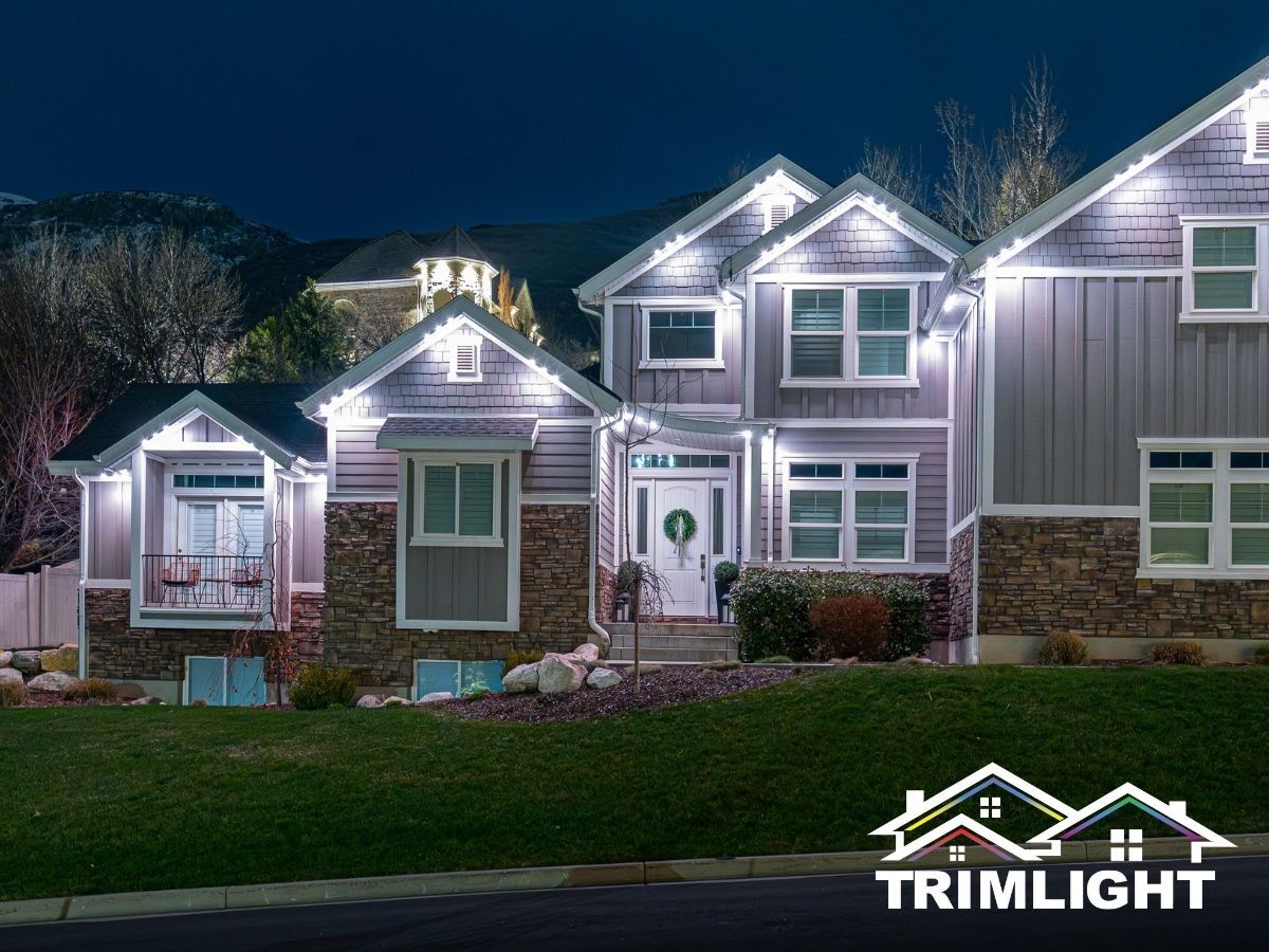 A house at night with white trim lights. The house has a stone facade and a green lawn.