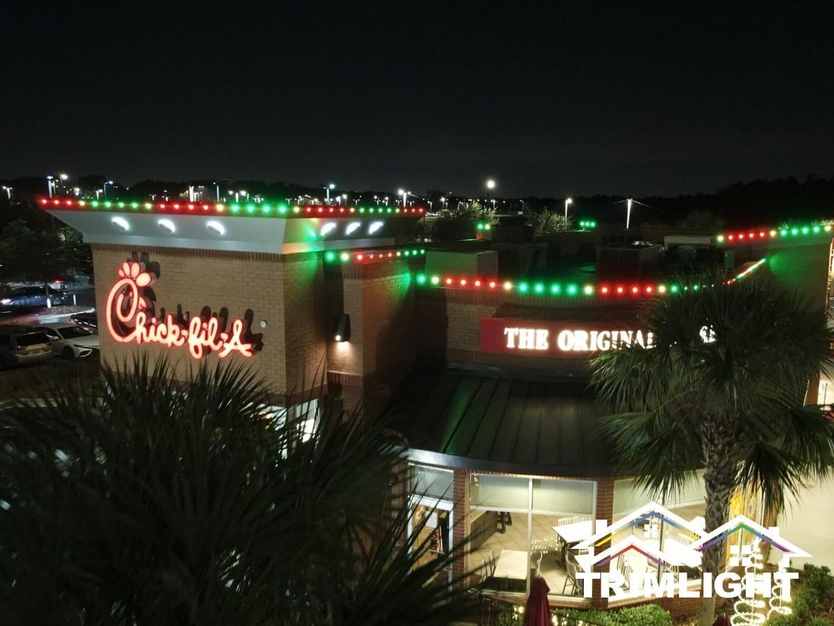 Chick-fil-A restaurant at night decorated with red and green lights. Palm trees in the foreground.