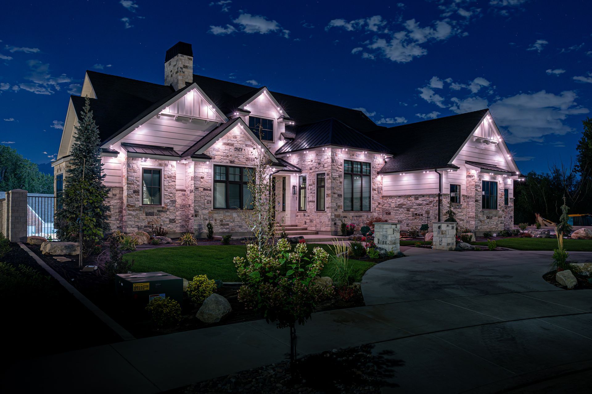 Illuminated stone house at night; landscape lights highlight the architecture against a starry sky.