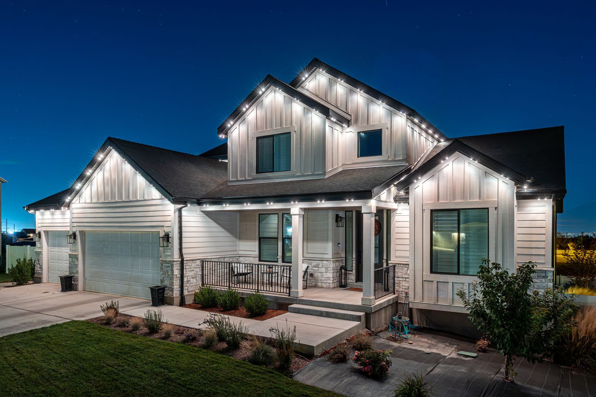White house with lit-up trim at night; lawn, driveway, and dark blue sky in the background.
