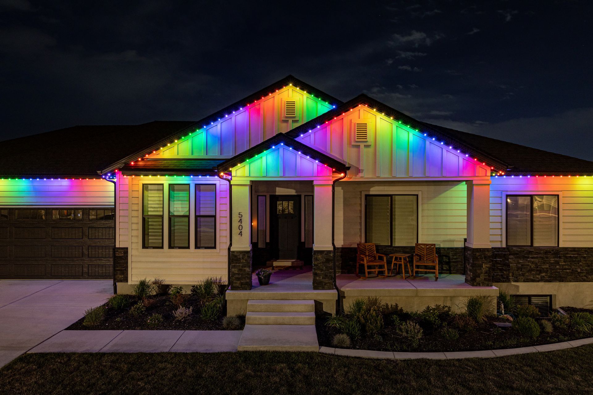 A house at night with rainbow-colored lights outlining the roof and porch.