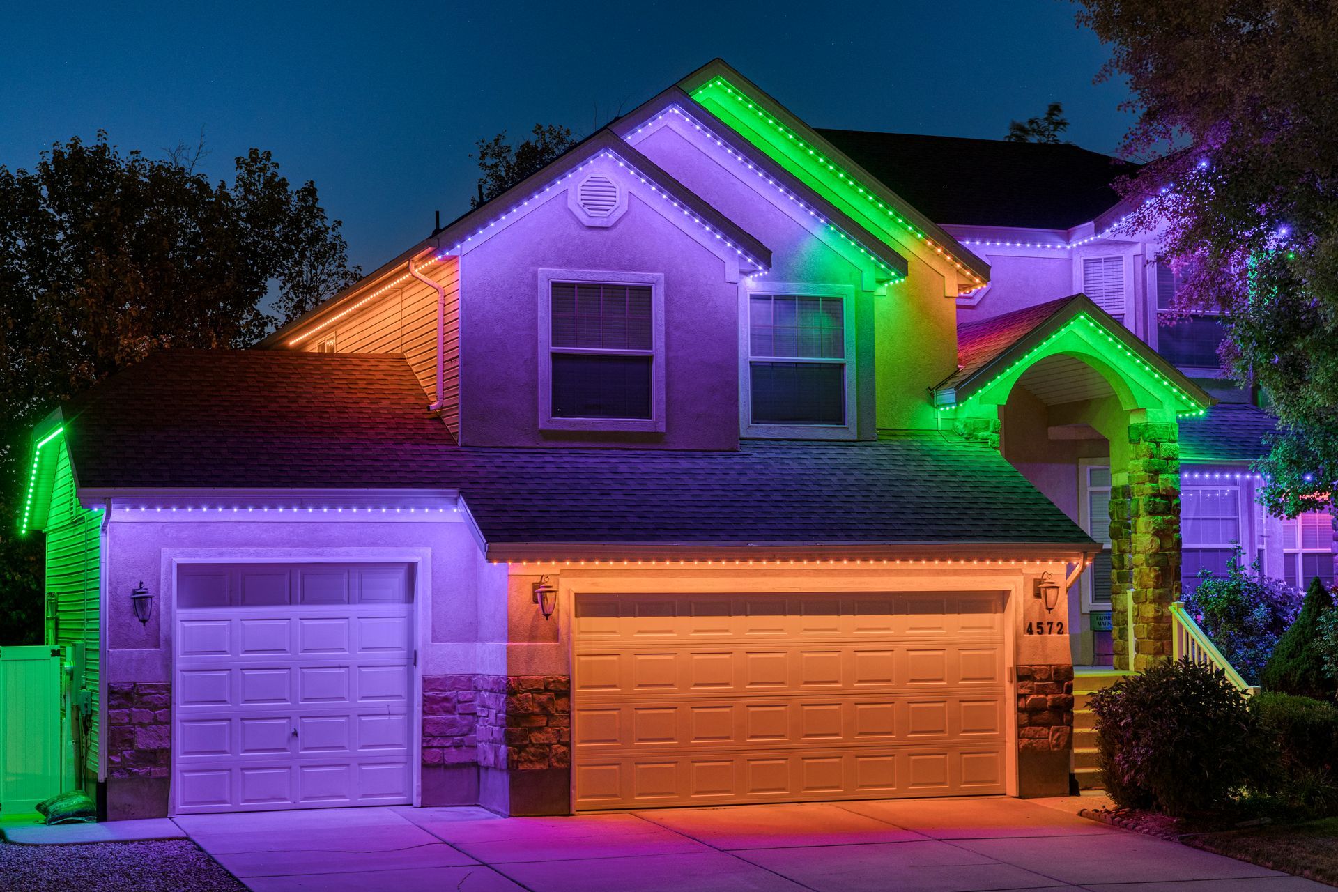 House exterior illuminated with green, purple, and orange lights at dusk.