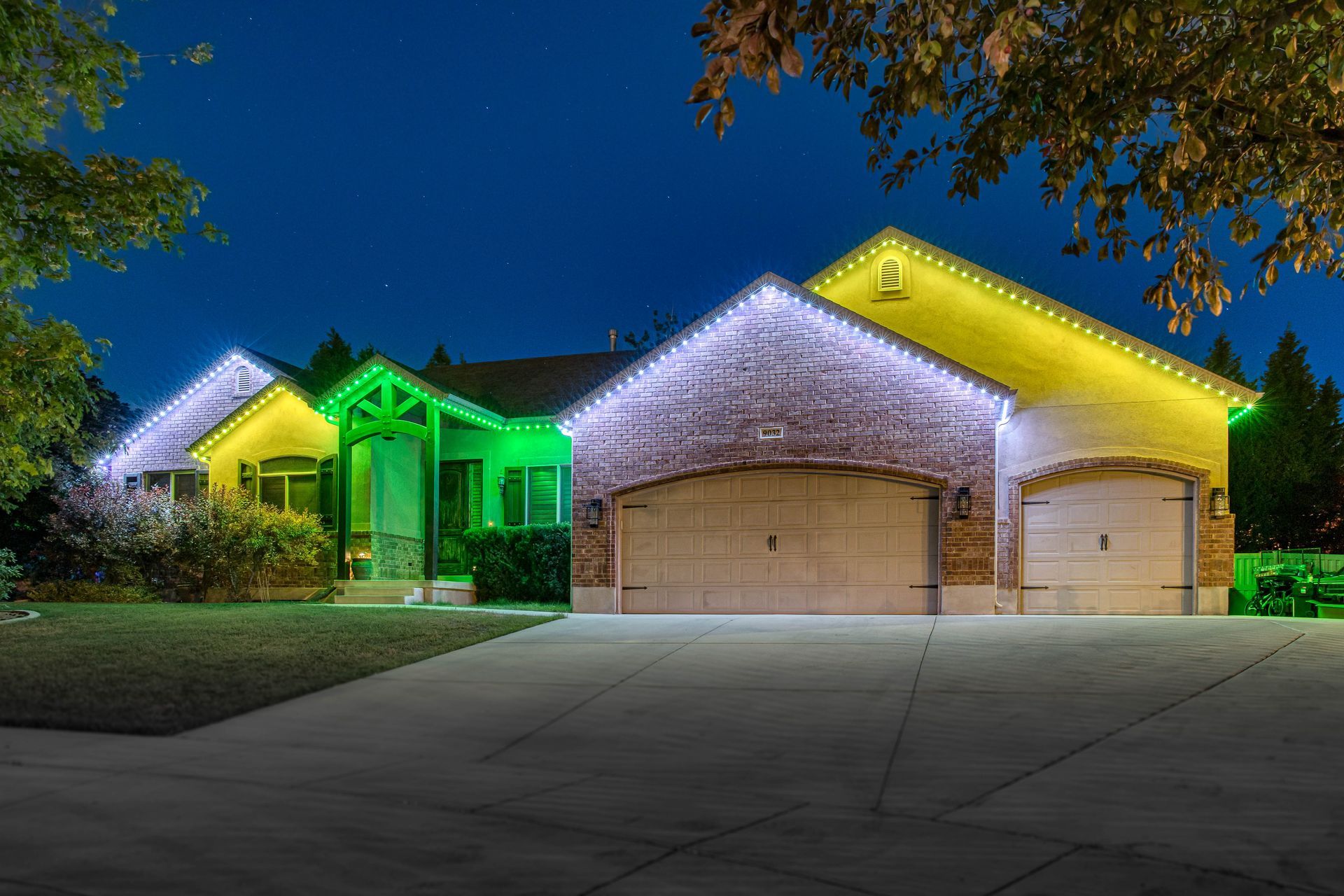 House decorated with green, white, and yellow Christmas lights against a night sky.