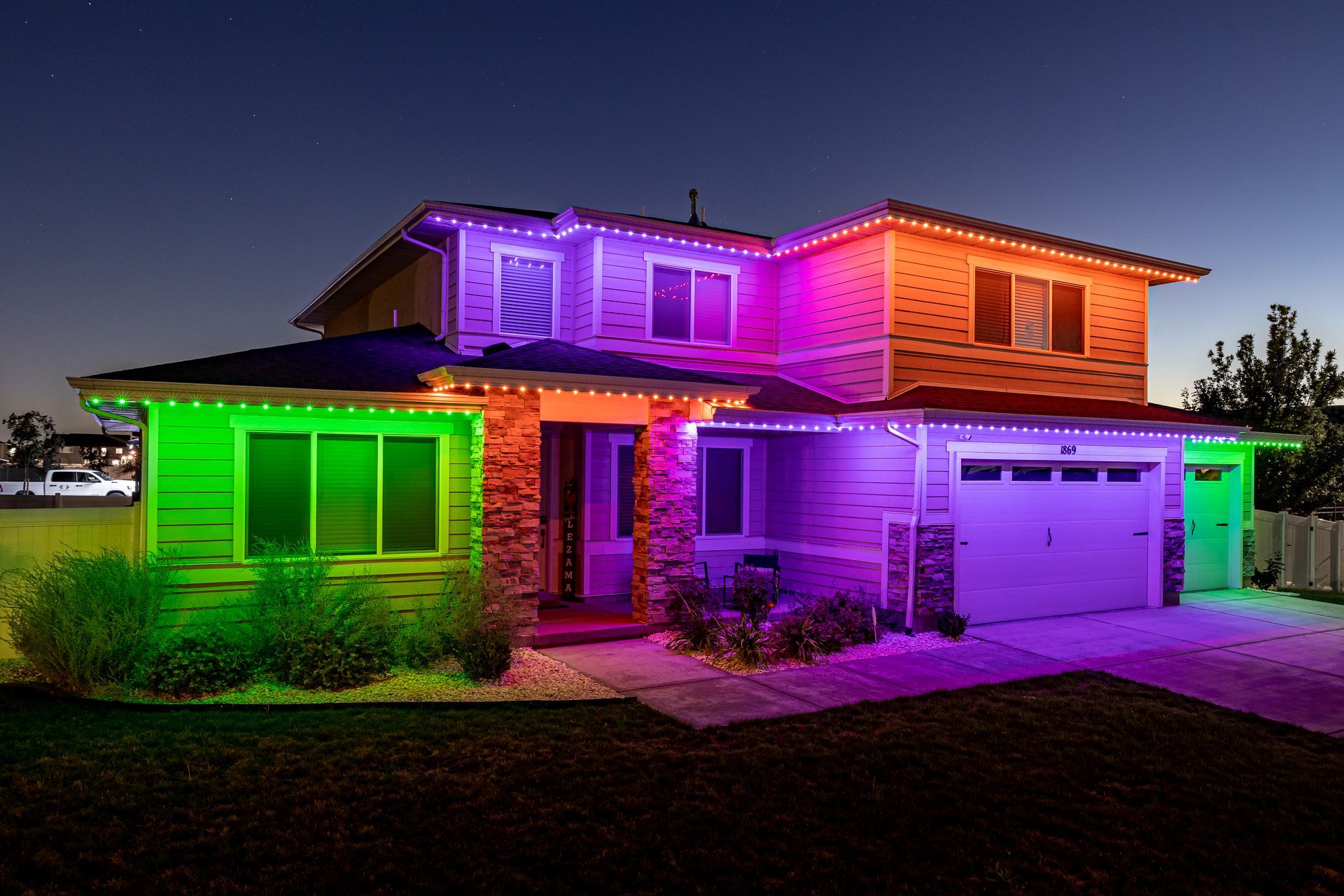 House exterior lit with colorful lights: green, purple, and orange. Nighttime setting.