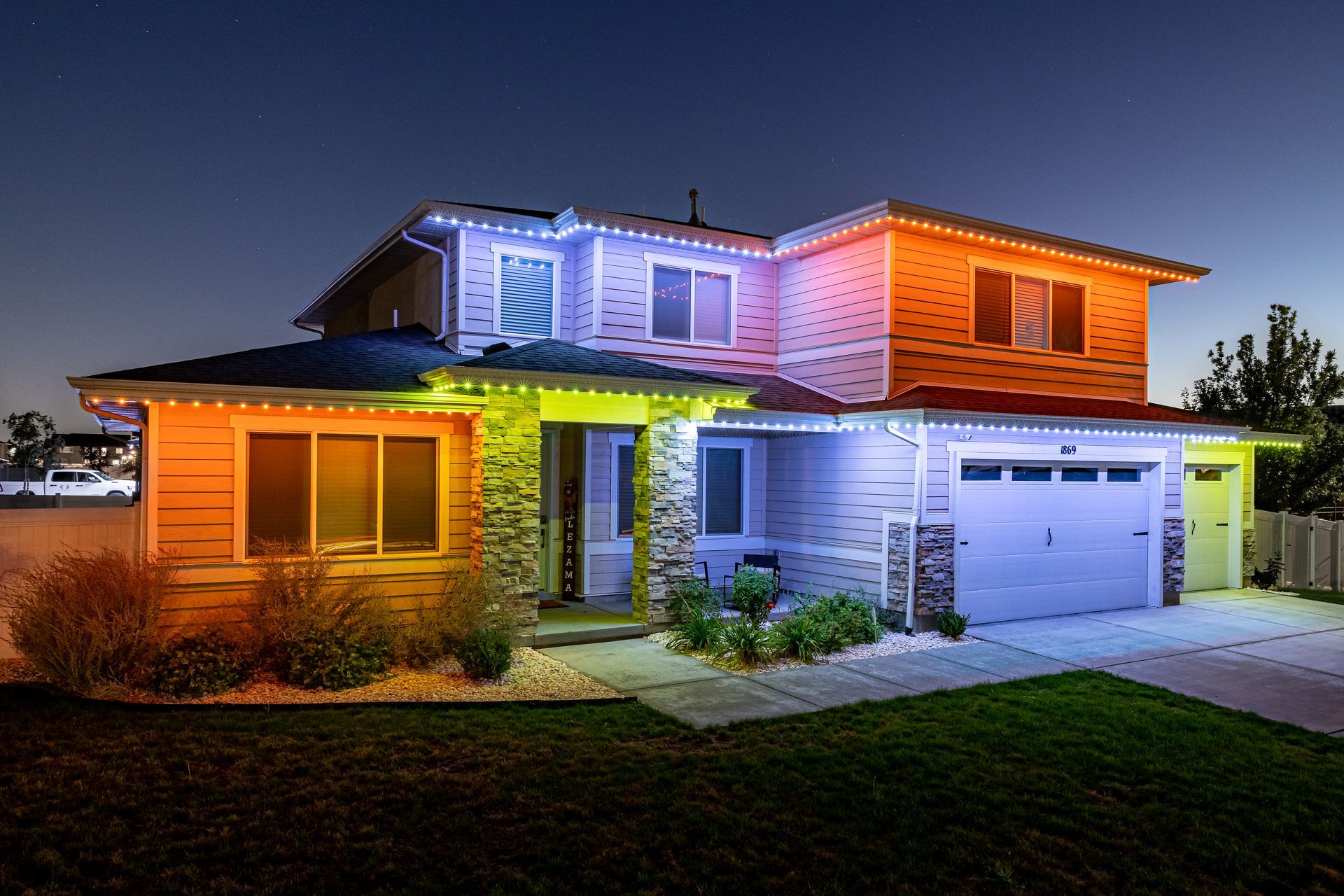 House exterior illuminated with colorful lights. Garage and roof lines accented with blue, orange, and green.