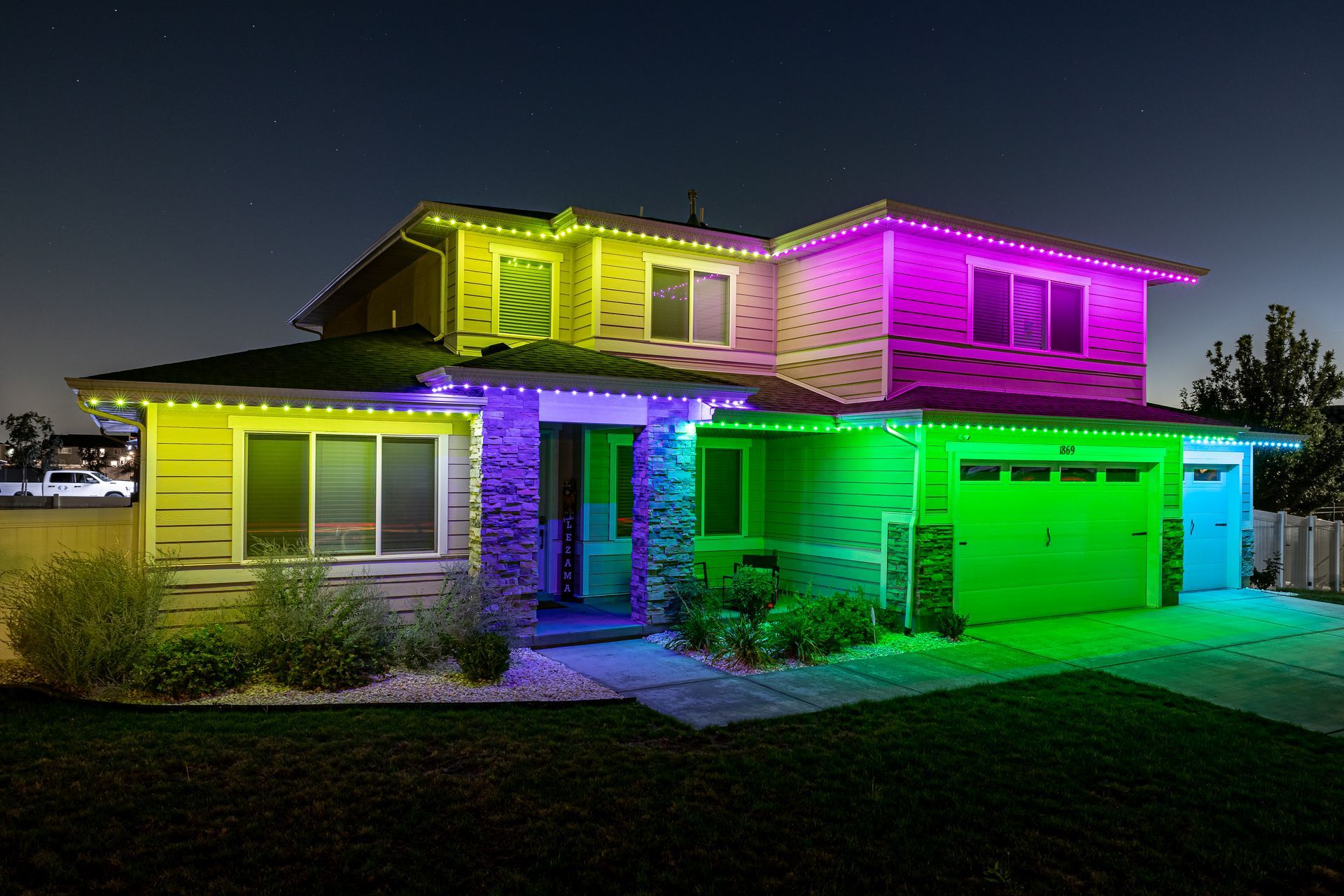 House with multi-colored lights outlining the roof and windows at night.