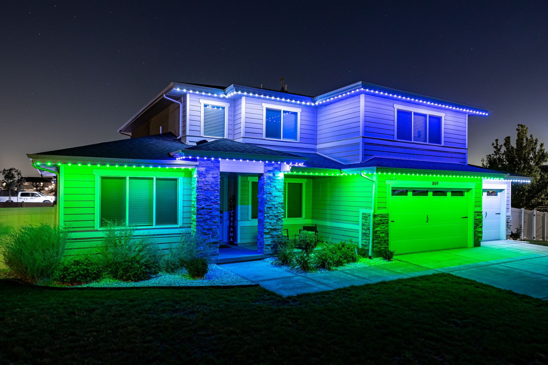 House decorated with green, blue, and white holiday lights at night.