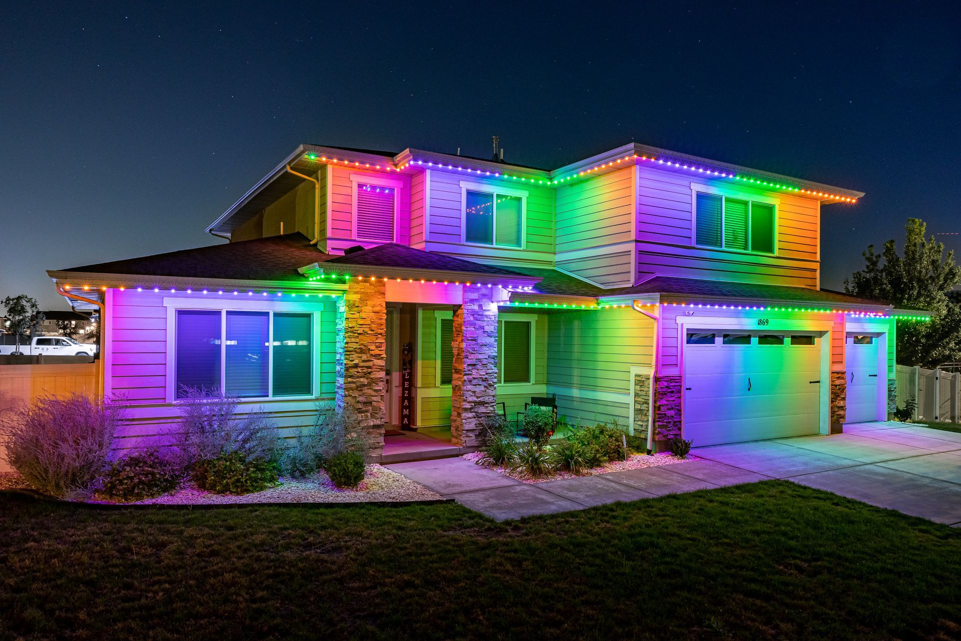 Two-story house with colorful, rainbow-colored lights outlining the roof and windows.