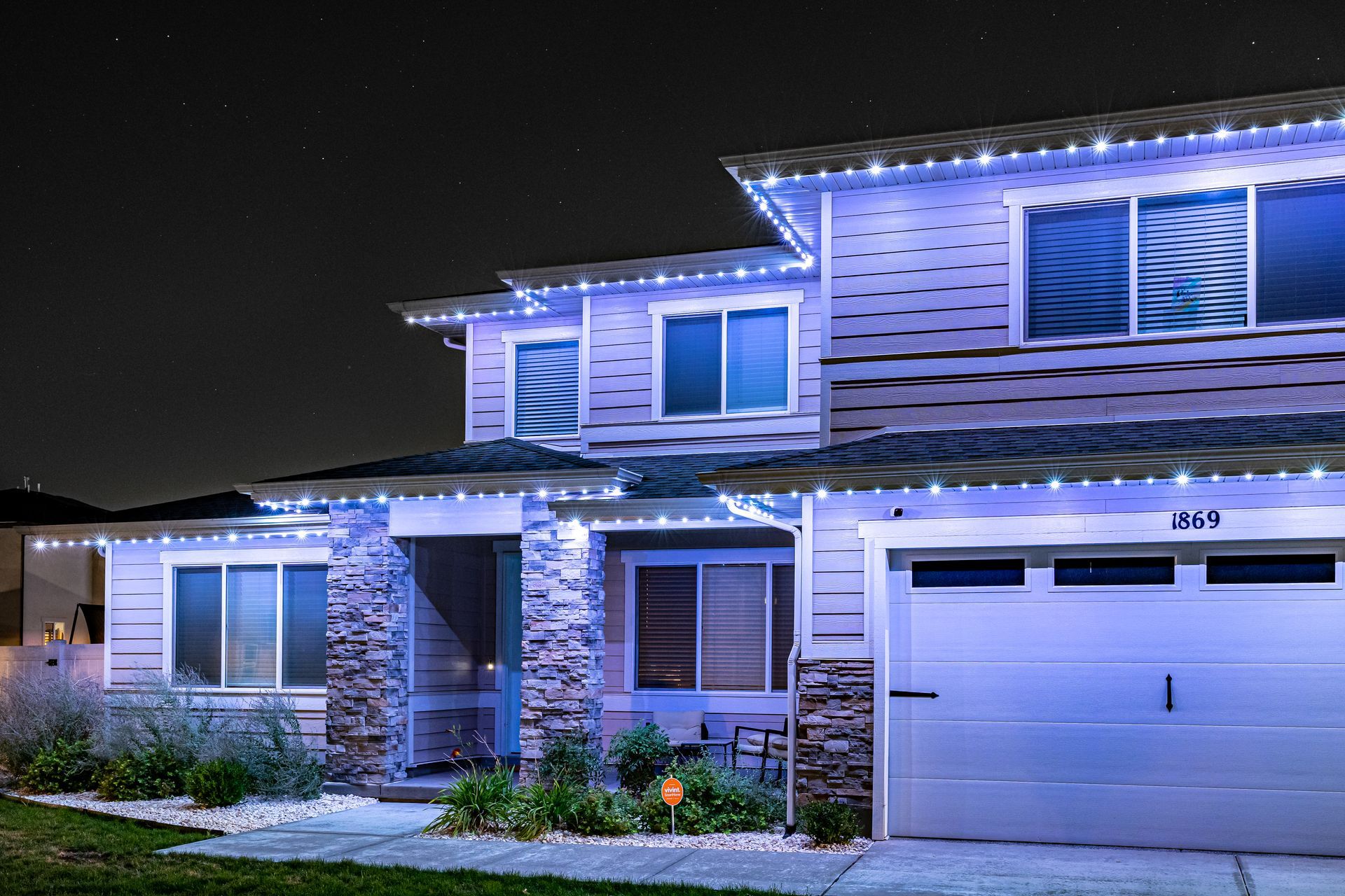 Two-story house with blue lights along the rooflines and above the garage at night.