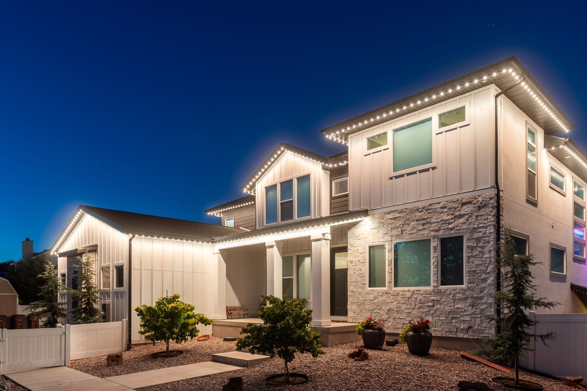 Modern two-story house illuminated with white lights against a dark blue sky.