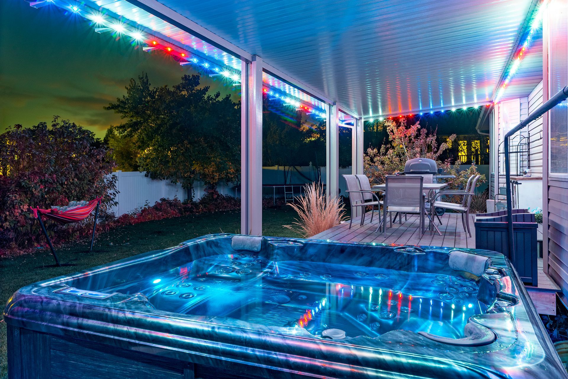 Hot tub lit with blue lights under a patio with string lights. Outdoor backyard setting at night.