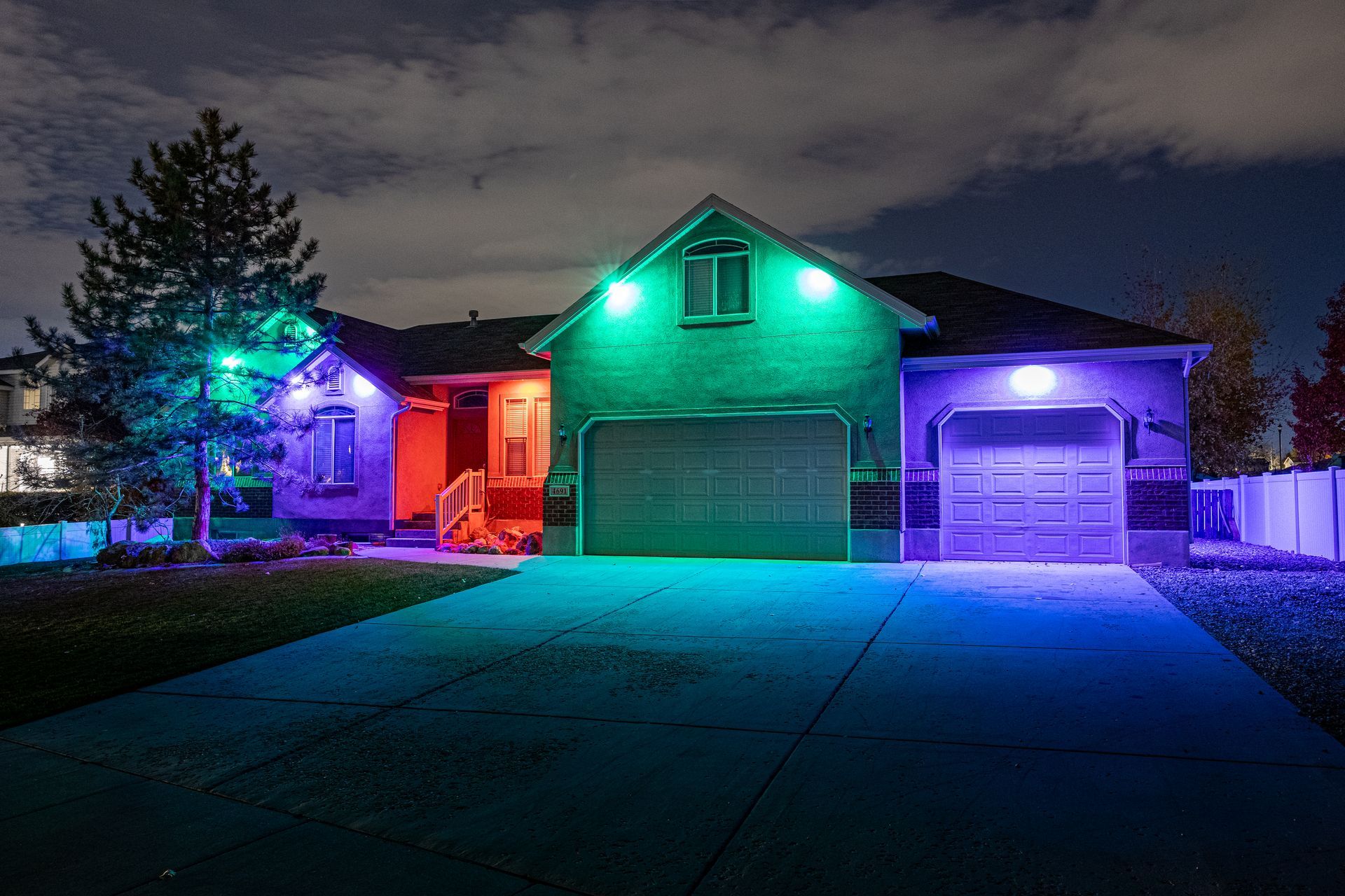 House at night illuminated with colorful lights, including blue, green, and red, on the roof and driveway.