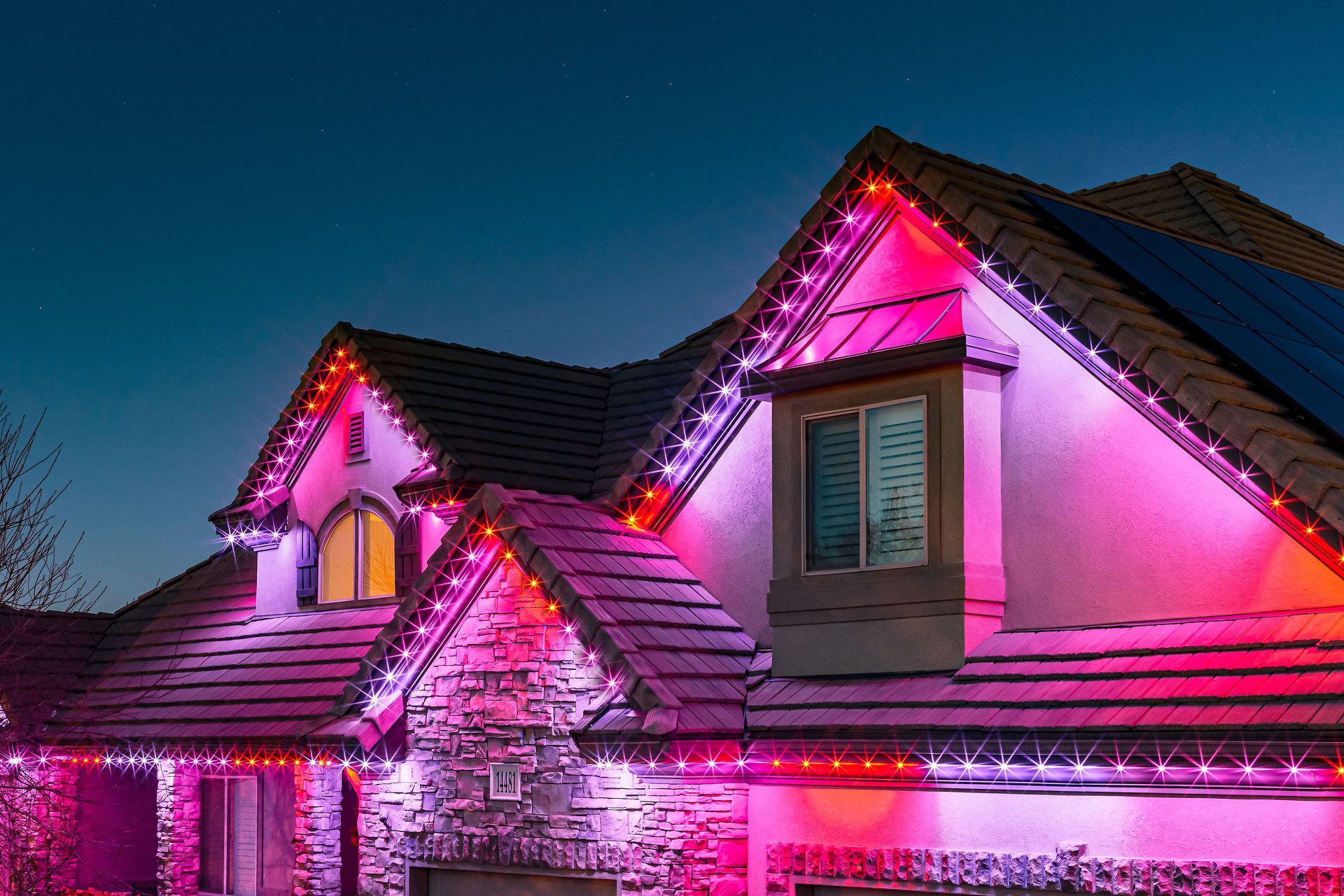 House exterior lit with pink, red, and purple Christmas lights. Roof and stone facade.
