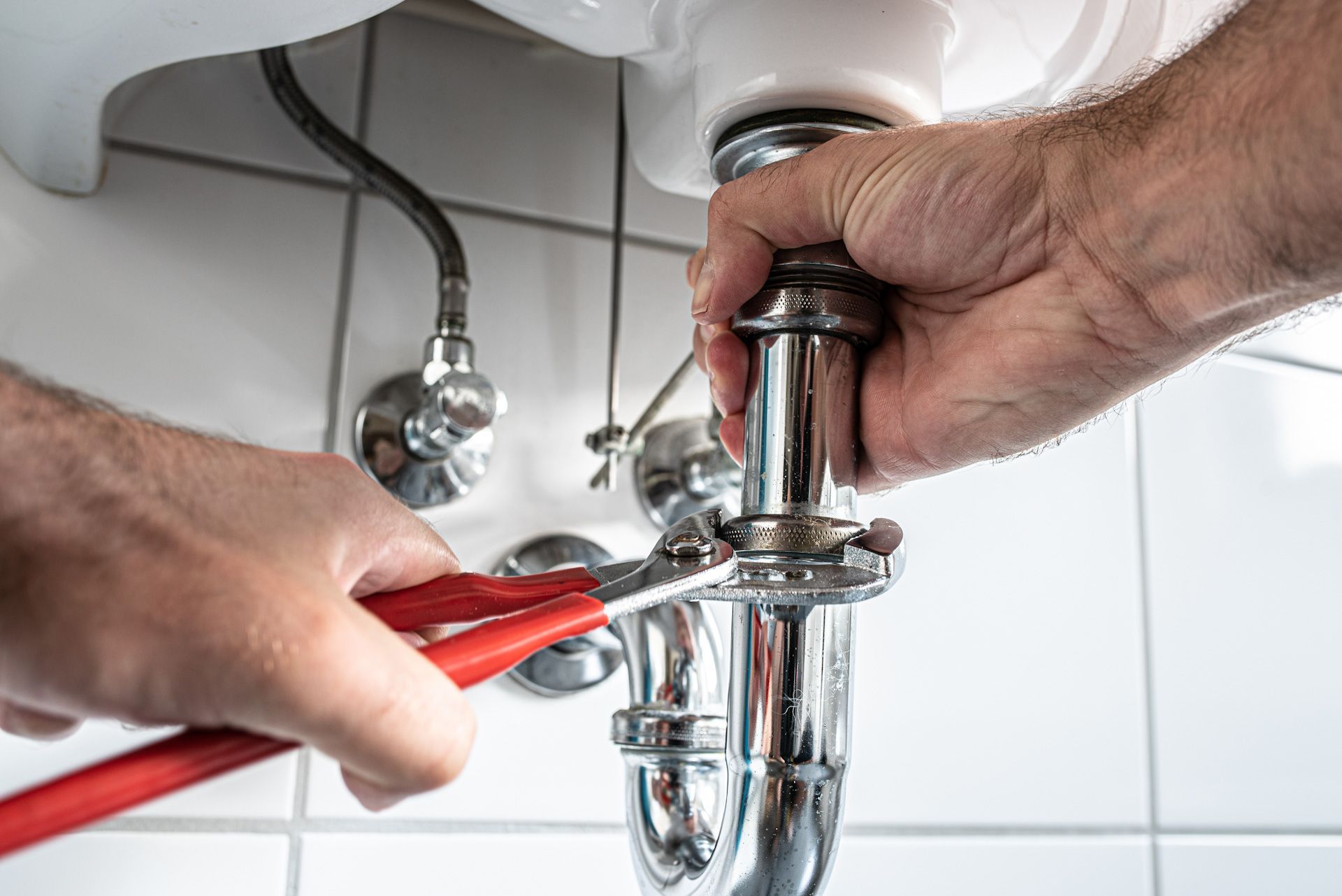 A plumber is fixing a sink pipe with a wrench.