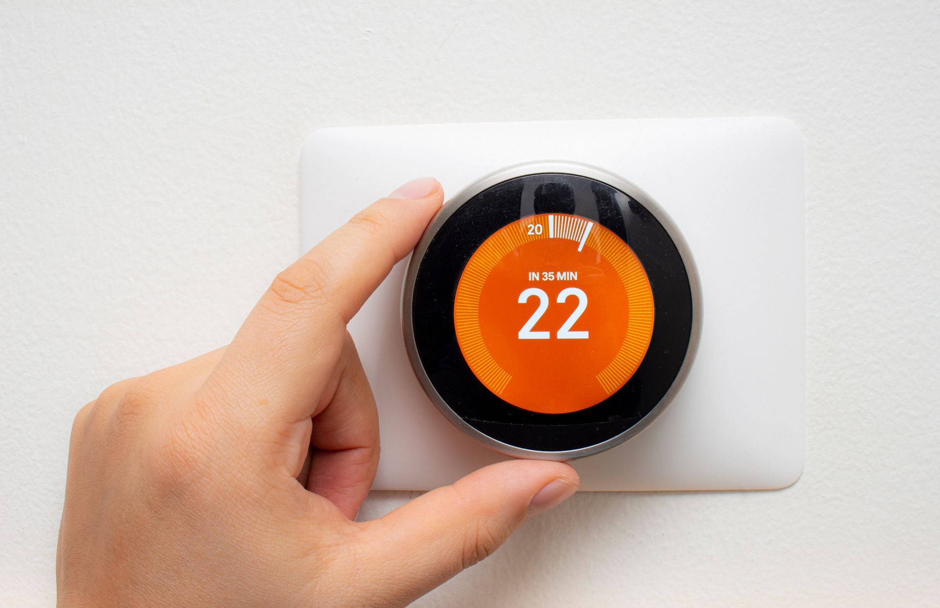A person is holding a smart thermostat in their hand.