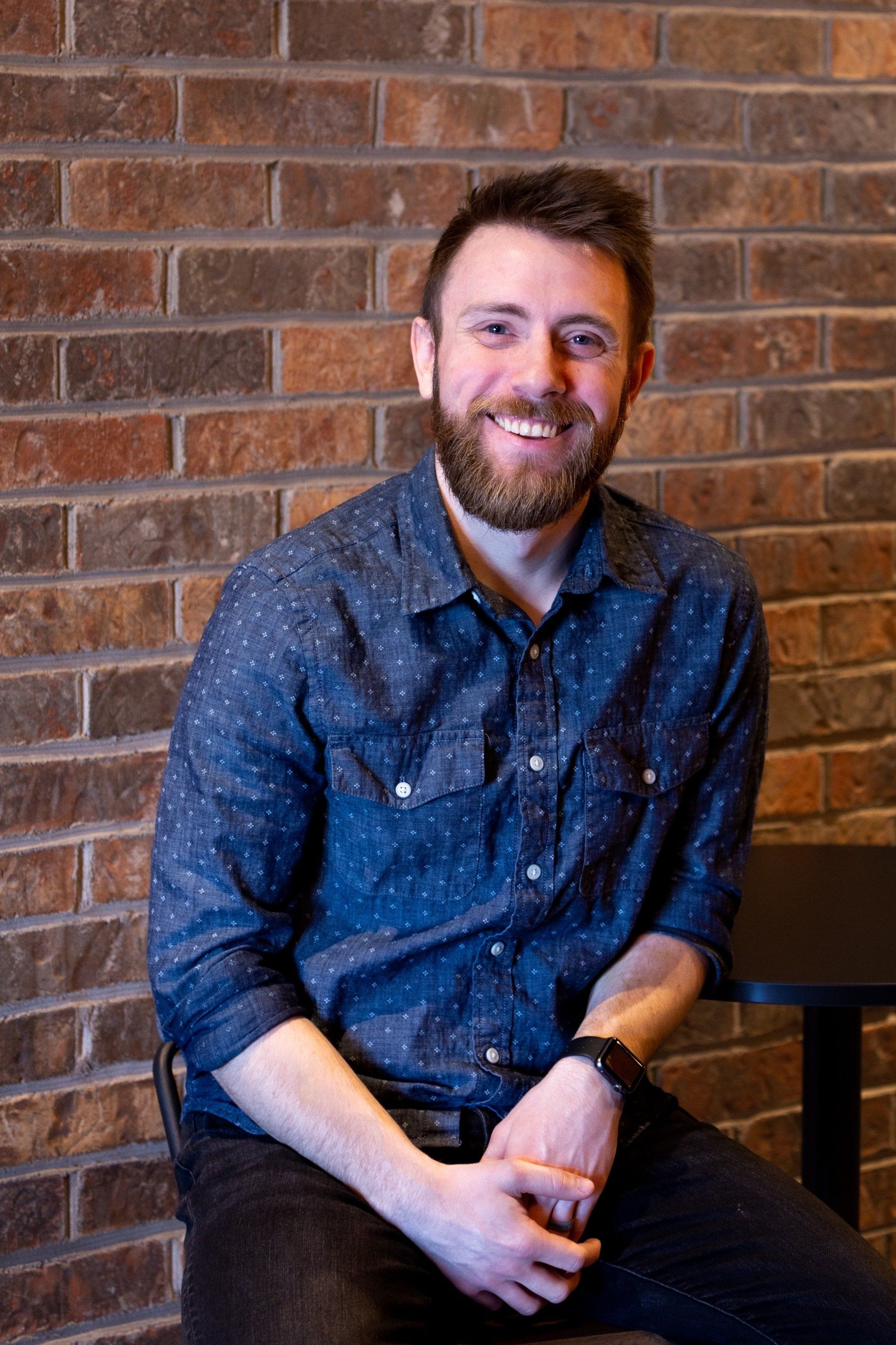 A man with a beard is sitting in front of a brick wall