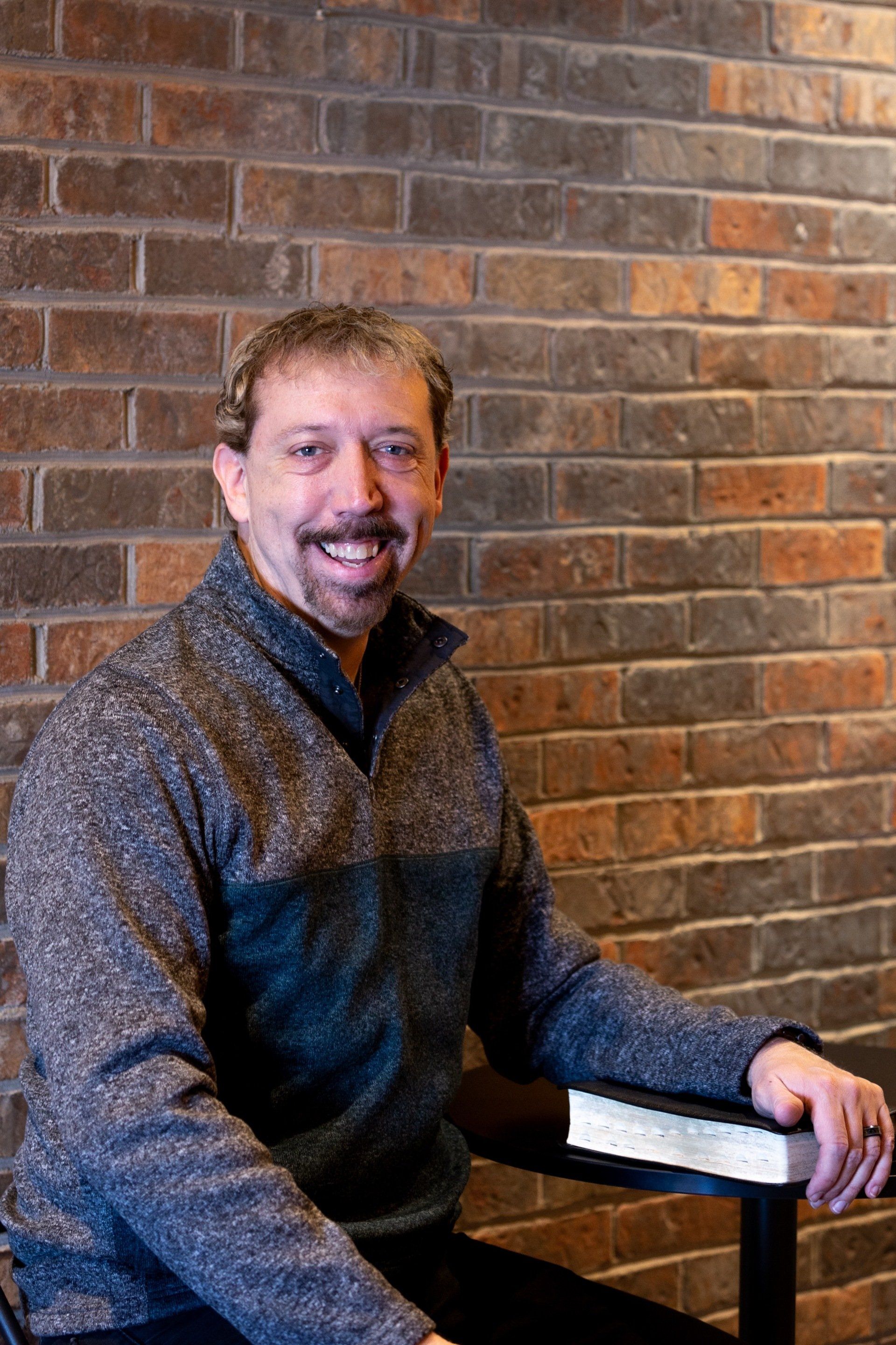 A man sitting in front of a brick wall holding a bible
