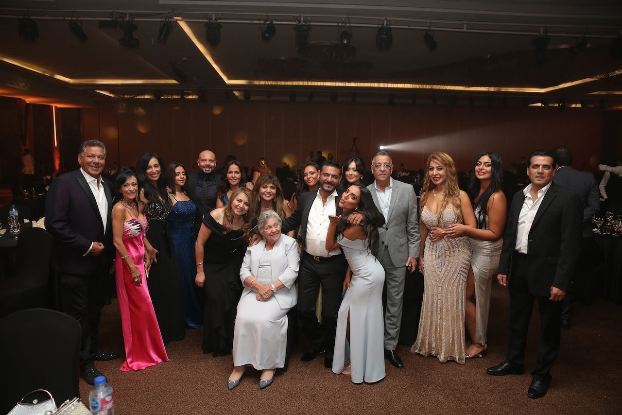 Group of people at an event pose for a photo. Well-dressed, indoor setting, some smiling.