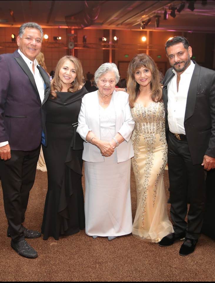 Five formally dressed people pose for a photo in an event space.