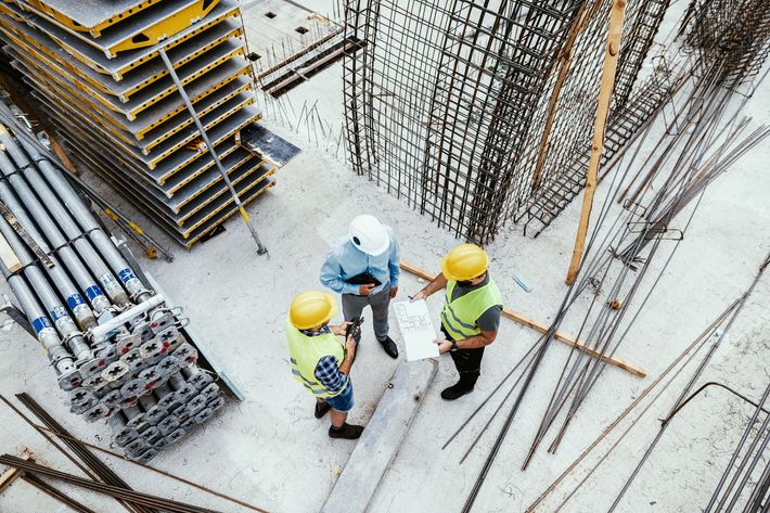 Un gruppo di operai edili è in piedi in un cantiere edile guardando un progetto.