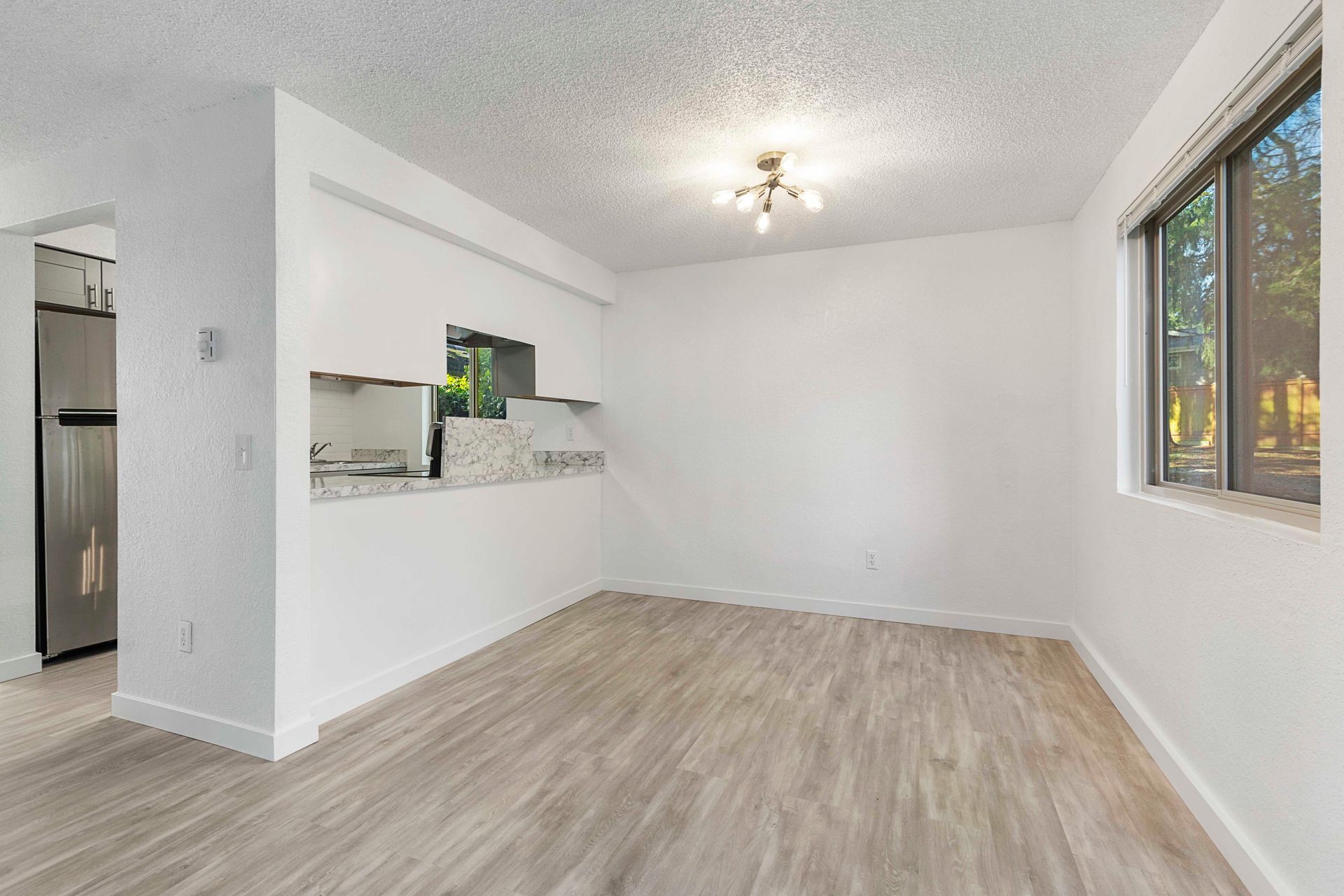 an empty living room with hardwood floors and a kitchen in the background .