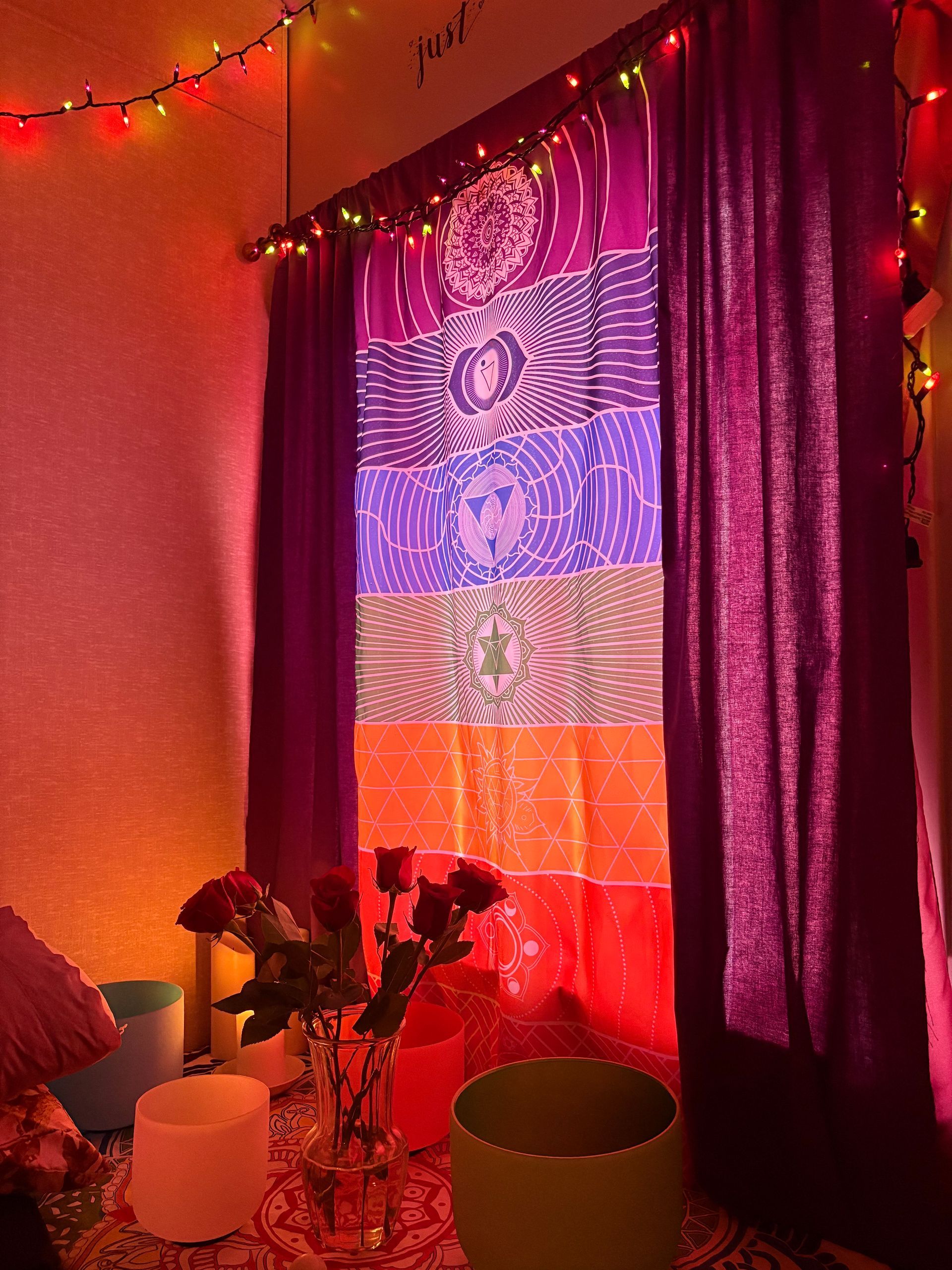 Colorful spiritual healing room with chakra-themed curtain, rose bouquet, candles, and singing bowls.