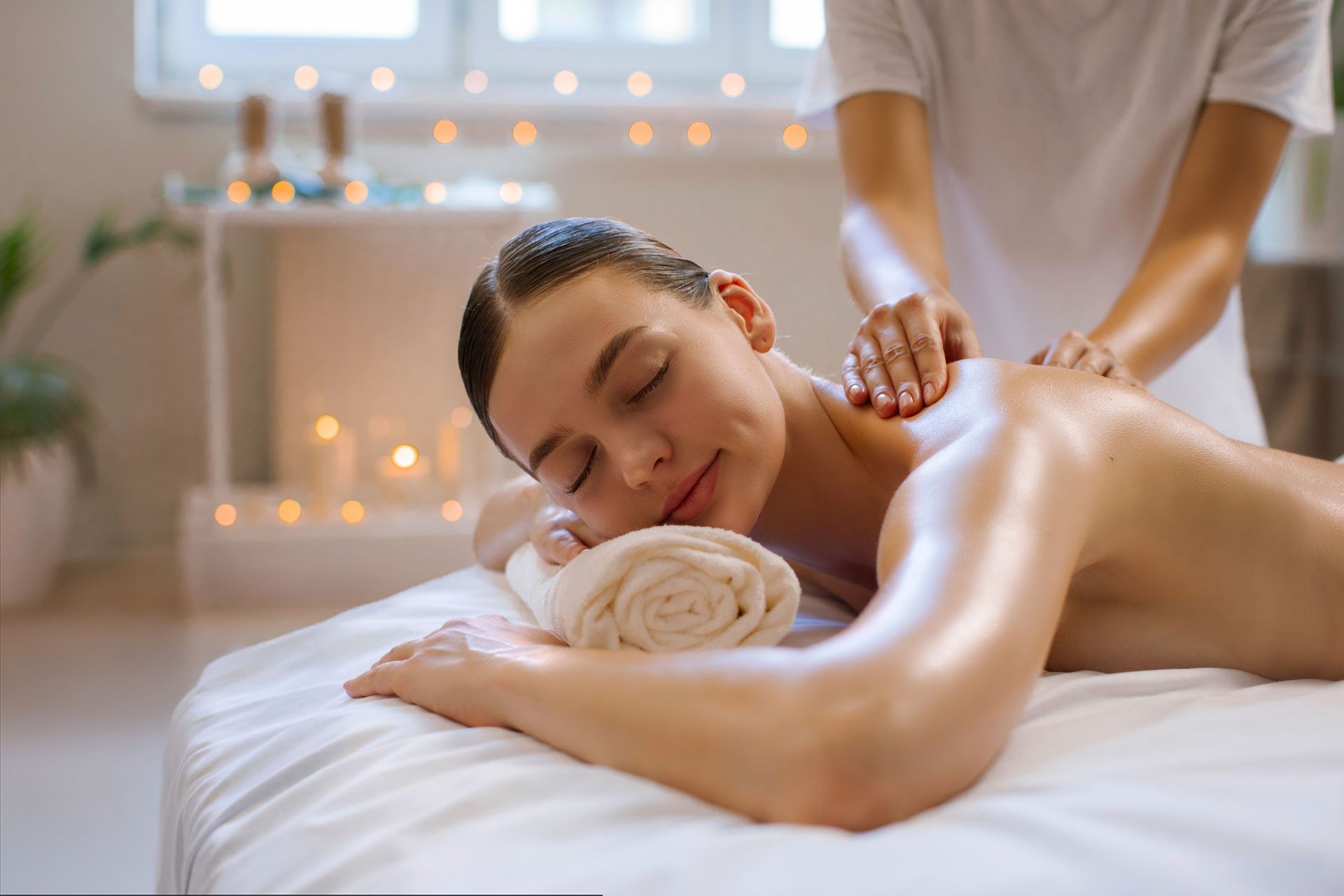 Woman receiving a back massage on a white massage table; hands pressing on her back.
