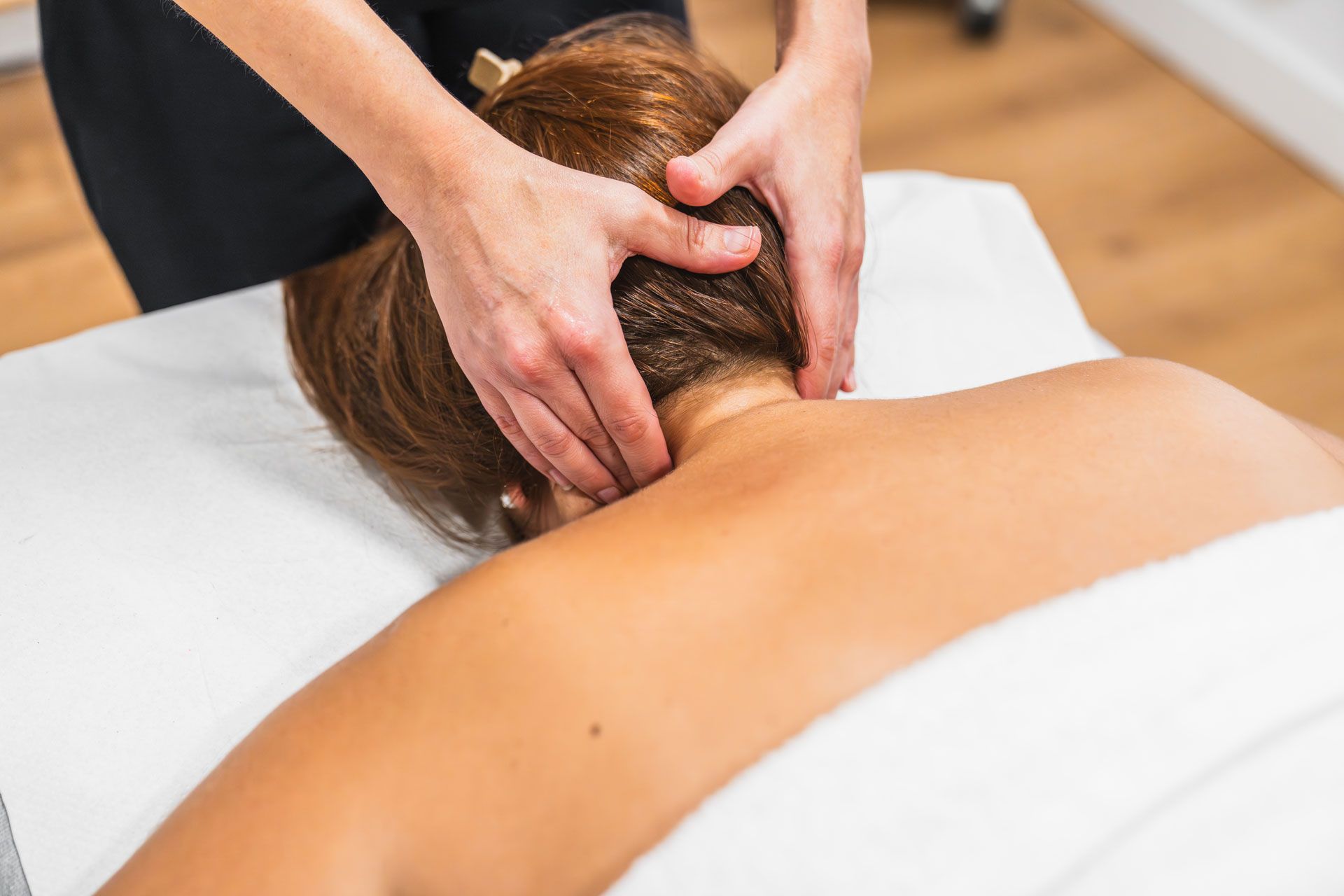 Hands massage the neck and scalp of a person lying face down on a massage table.