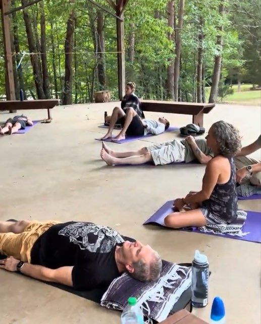 Woman meditates in a lotus position on a mat, eyes closed, hands in mudra, in a sunny living room.