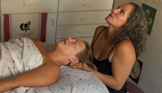 Woman receiving reiki therapy with hands over her head, eyes closed.