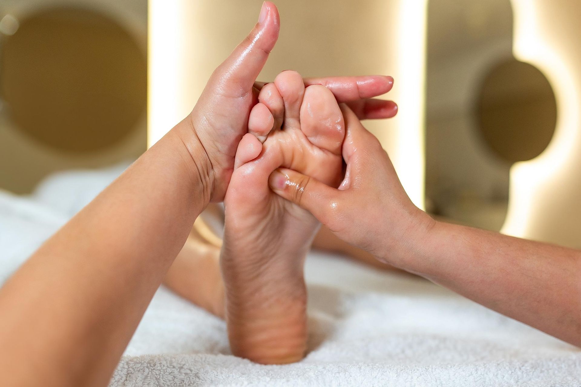 Hands massaging the sole of a foot, indoors, likely at a spa.