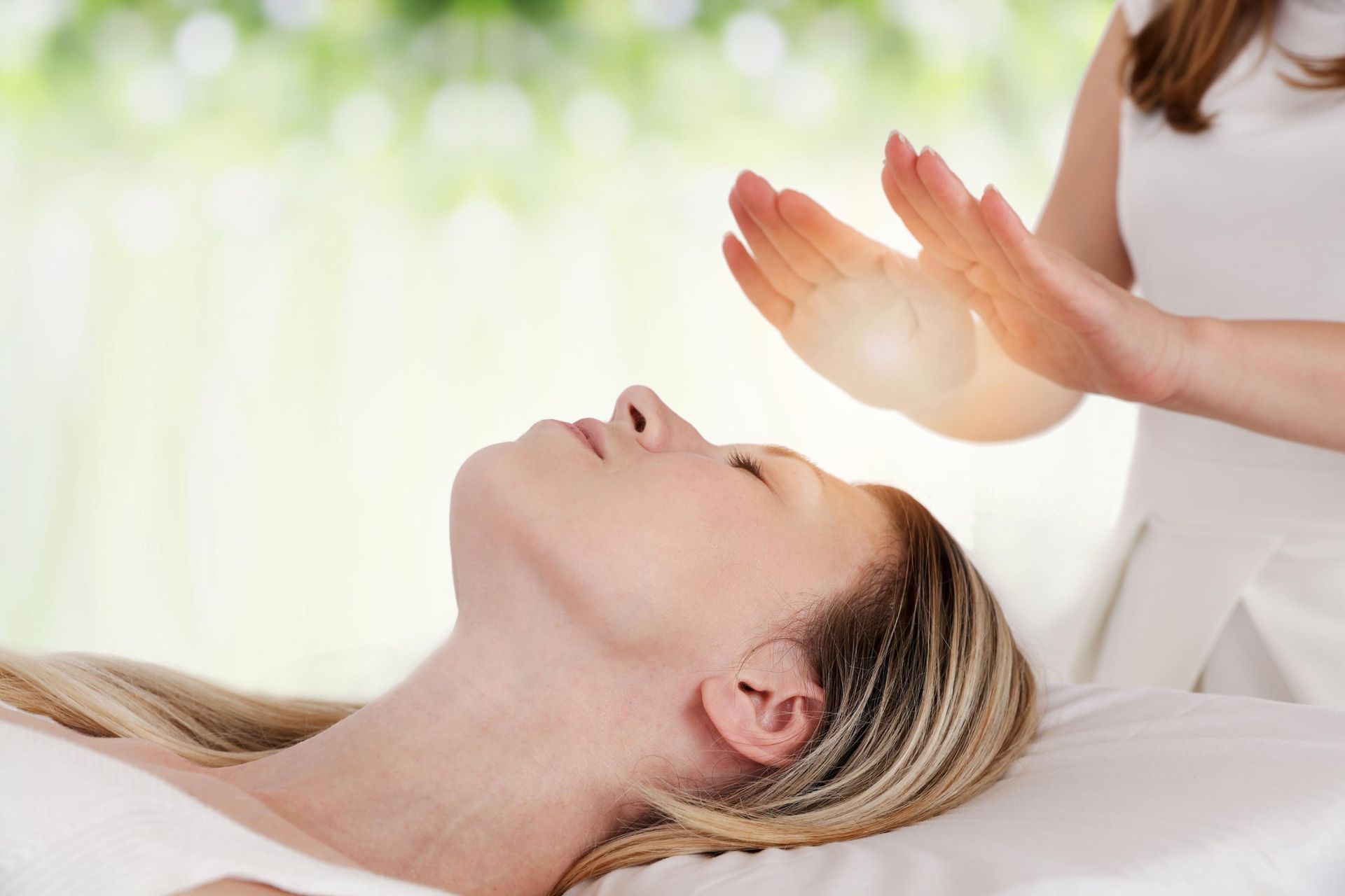Person receiving reiki treatment, hands glowing, soft light, serene expression, outdoors background.