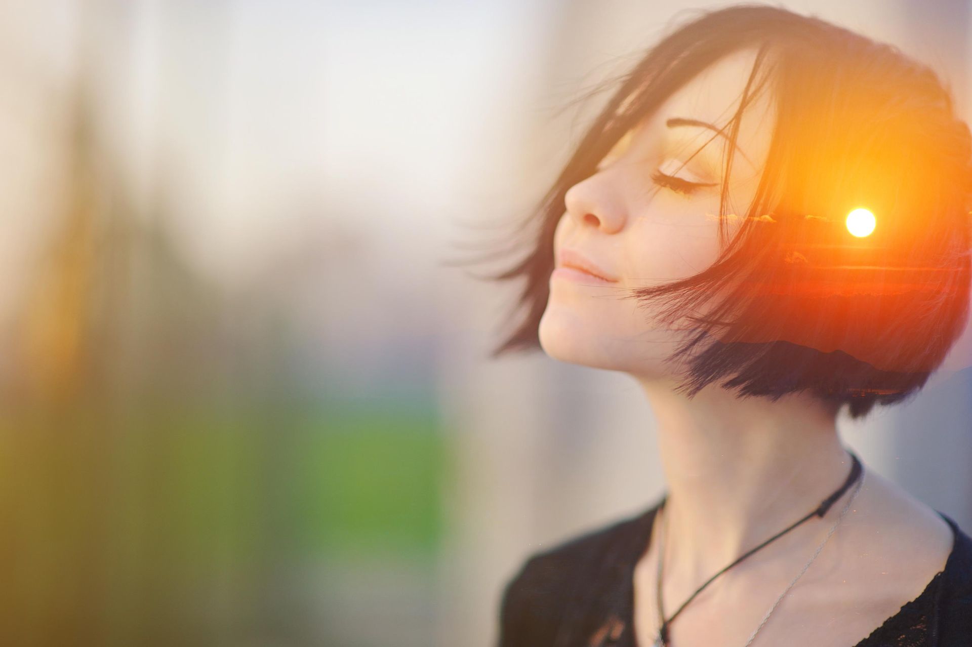 Woman with short dark hair, eyes closed, superimposed with a sunset.