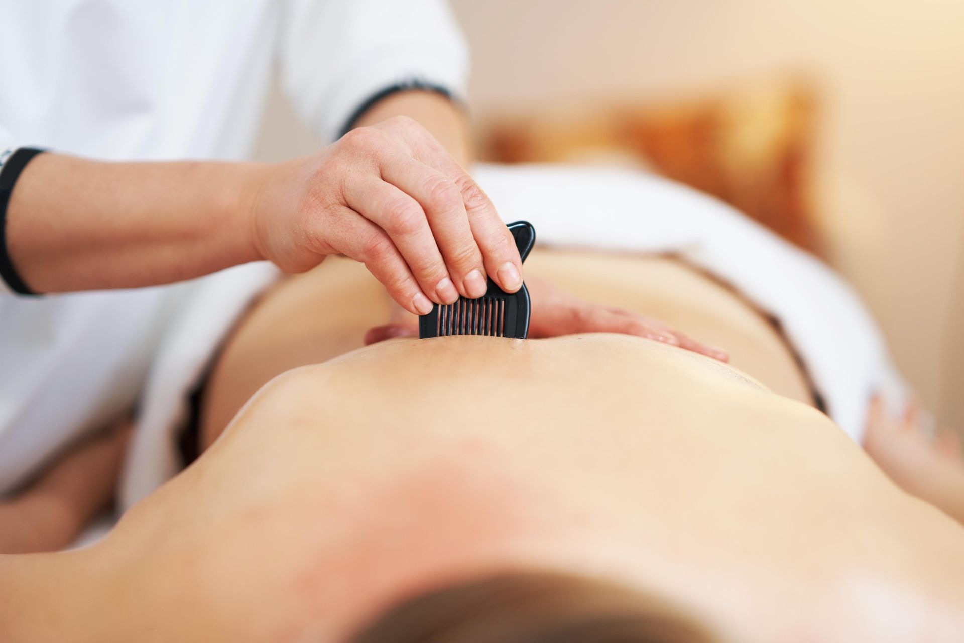 Person receiving a back massage with small, dark tools in a spa-like setting.