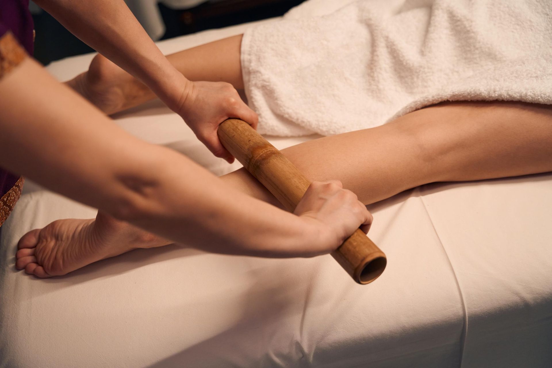 Leg being massaged with a bamboo stick on a massage table, in a spa.