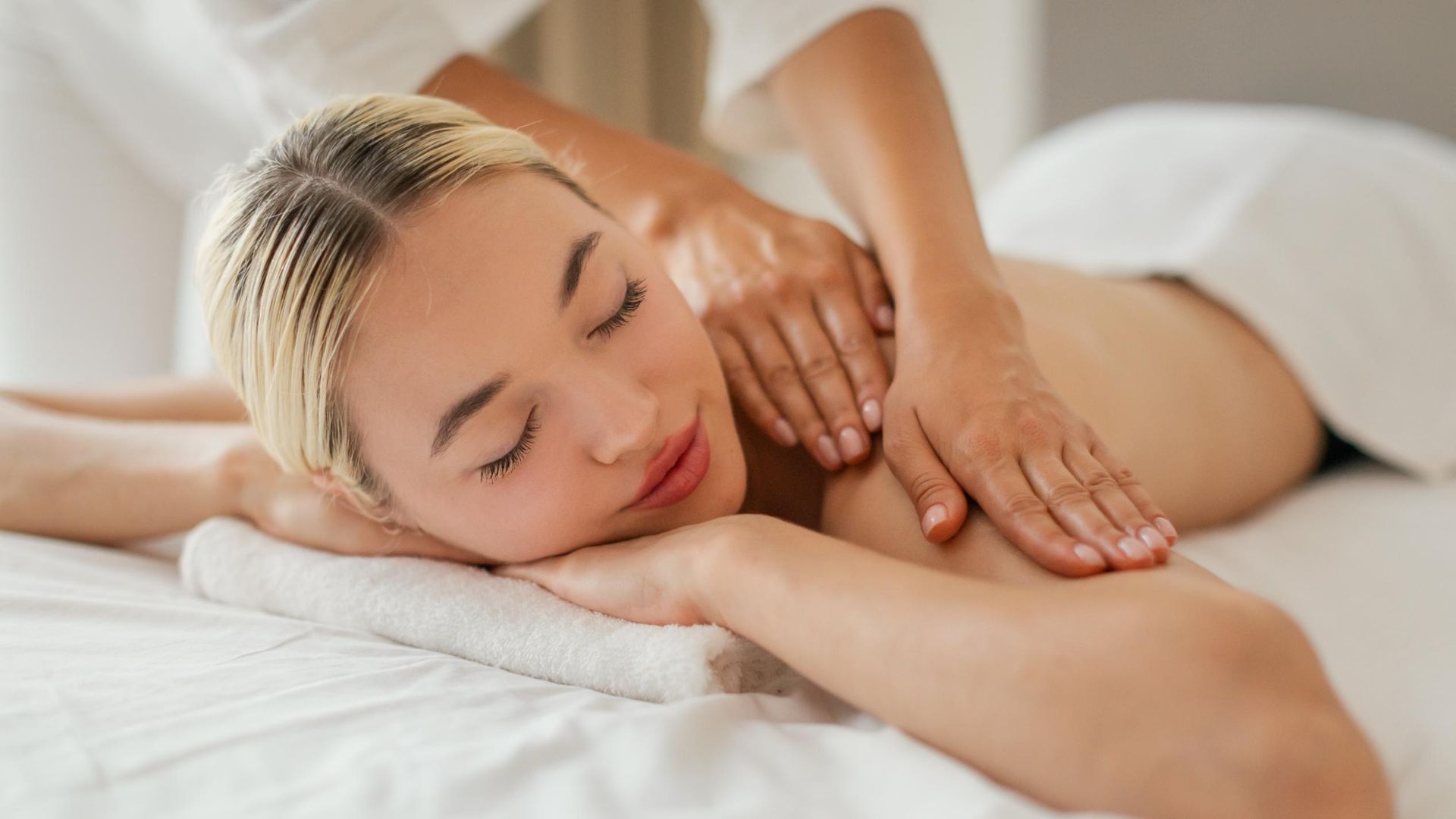 Woman receiving a back massage on a white massage table; hands pressing on her back.