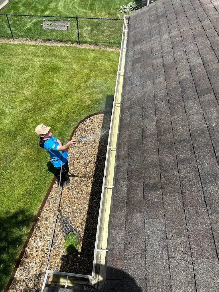 A man is cleaning a gutter on the roof of a house.
