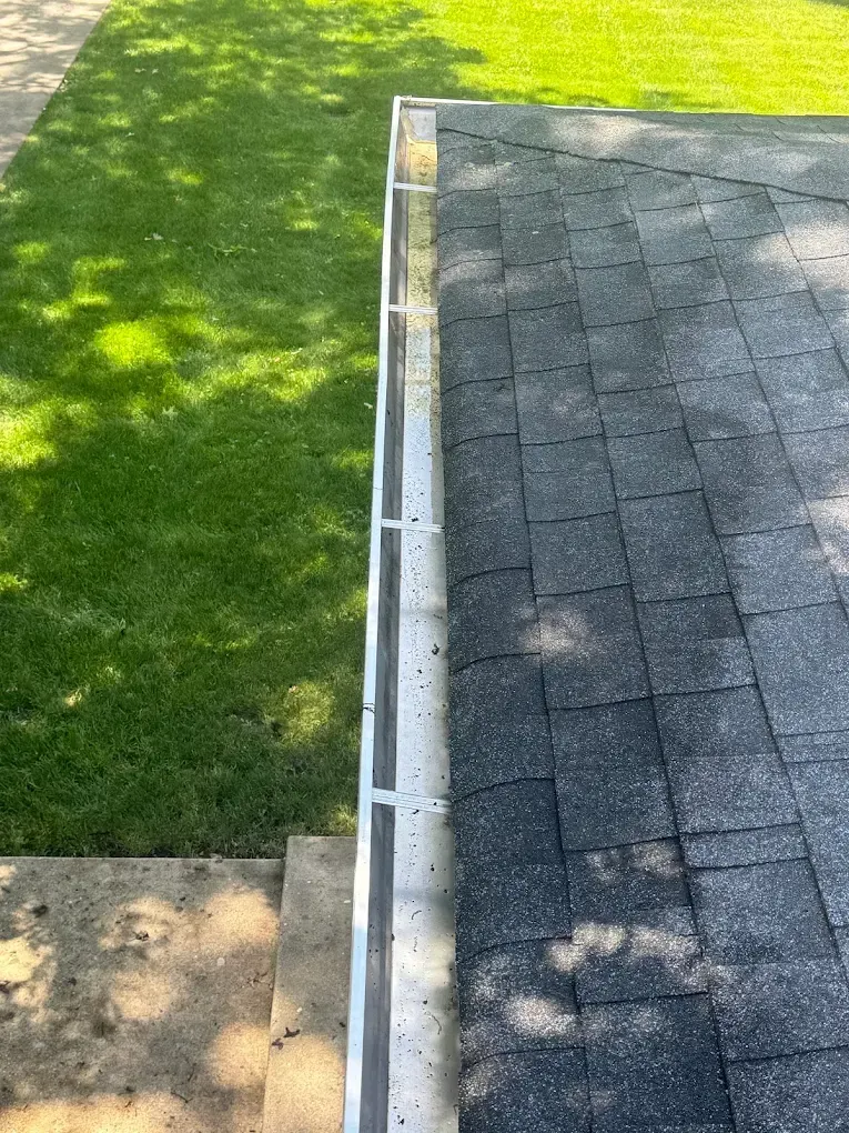 A gutter on a roof next to a lush green lawn.