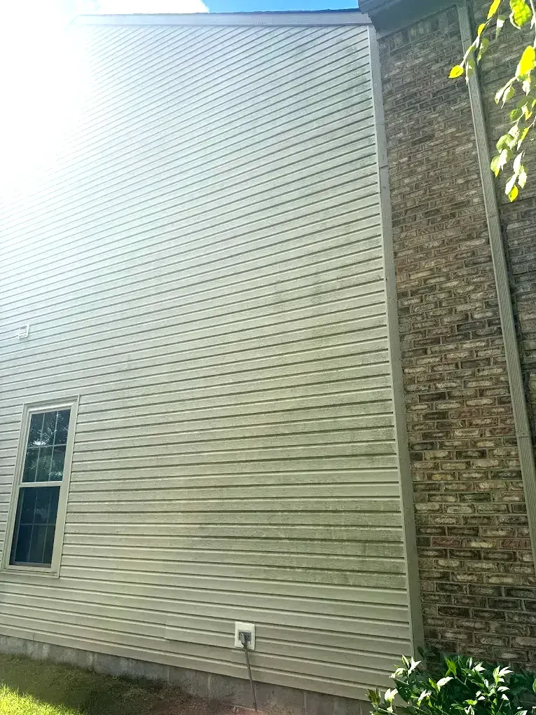 The side of a brick house with a white siding and a window.