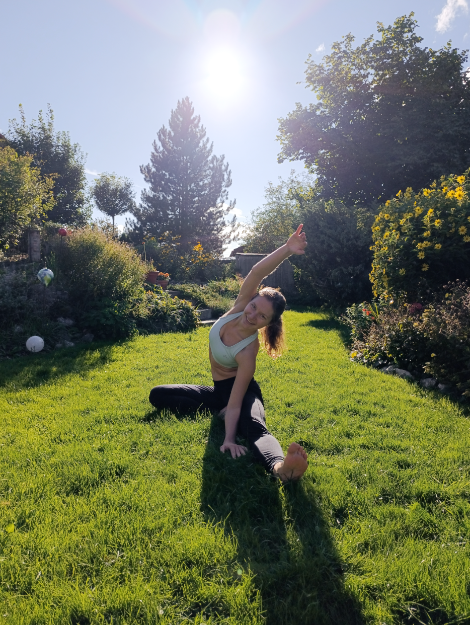 Frau in Sportkleidung macht seitliche Dehnungen auf grünem Gras in einem sonnigen Garten.