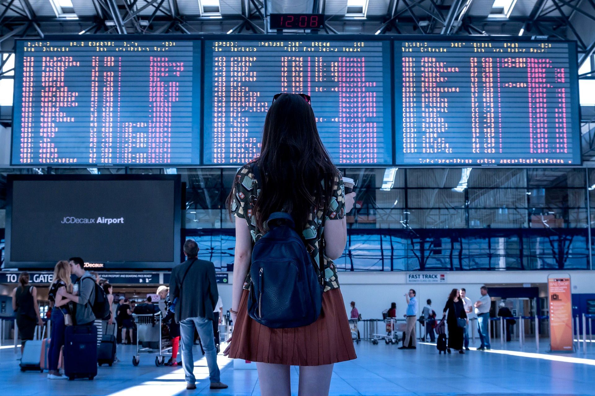 Une femme avec un sac à dos se tient devant le panneau des départs d'un aéroport.