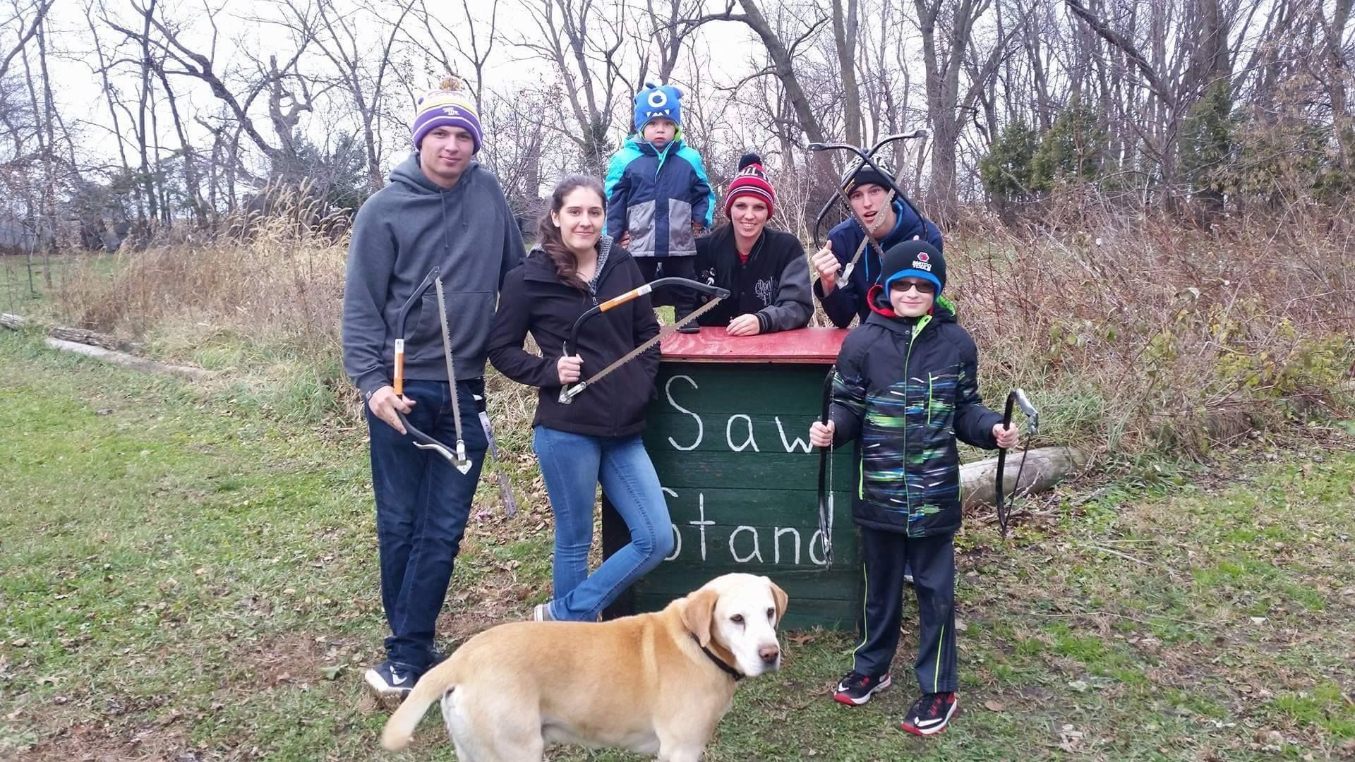 A group of people standing in front of a sign that says saw stand on their way to go out and pick a tree.